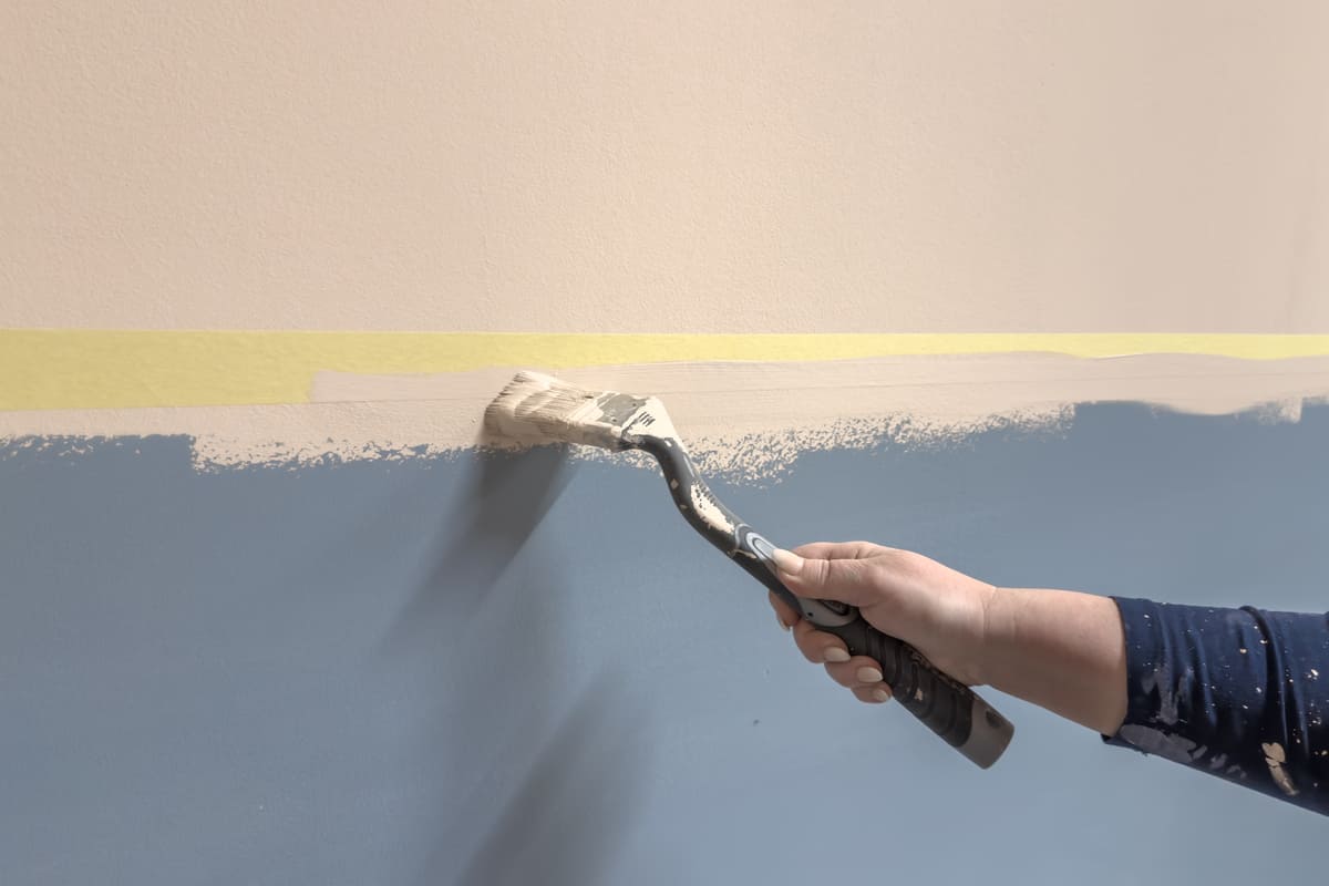 En person målar en vägg blå med en pensel.