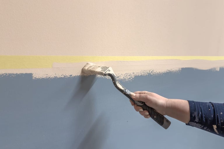 En person målar en vägg blå med en pensel.