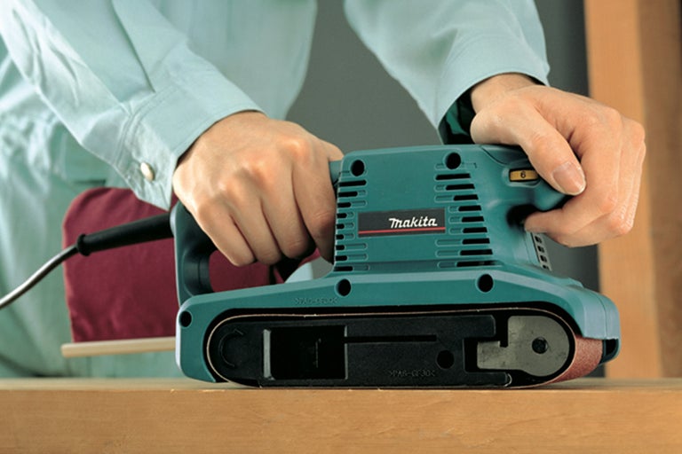 Makita bandslipmaskin används på en träyta.