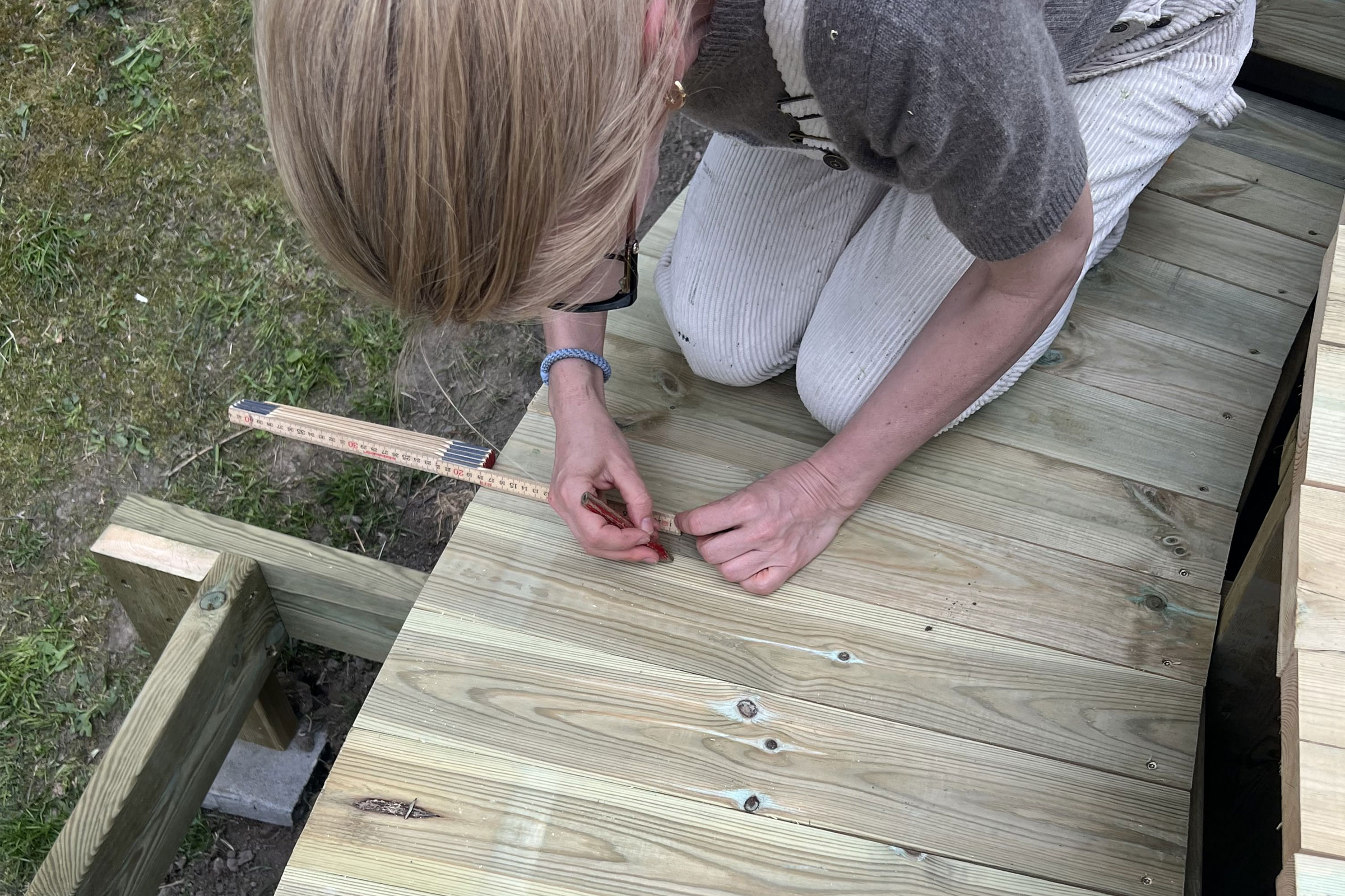 Kvinna mäter ett trädäck med en tumstock och en penna.
