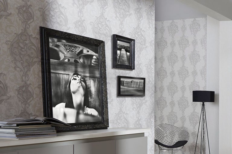 Dekorativt vardagsrum med mönstrad tapet, lampa, stol och flera inramade bilder