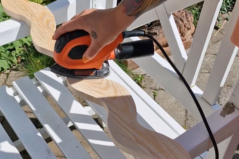 En person slipar en träbit med en Black and Decker slipmaskin på en vit bänk.