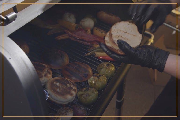 Bröd, lök, paprika och bacon tillagas på en grill.