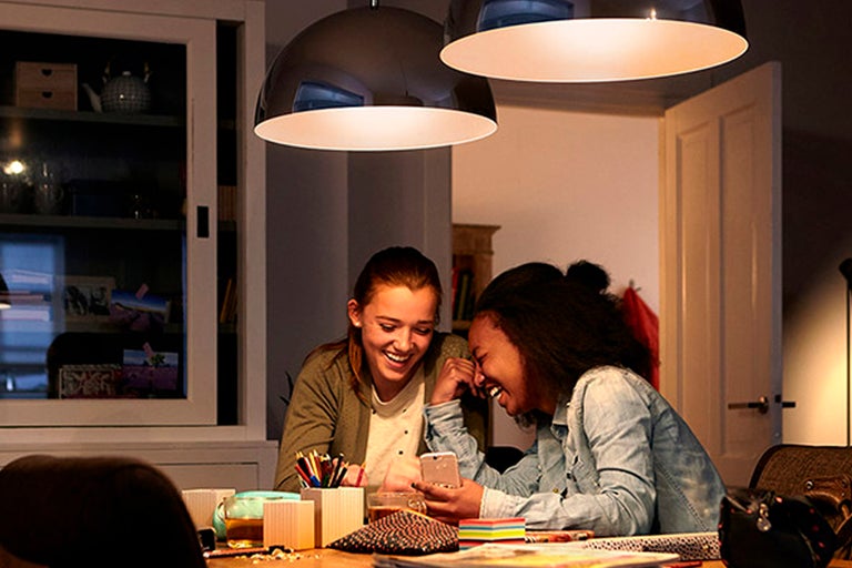 Två unga kvinnor skrattar vid ett bord under hänglampor.