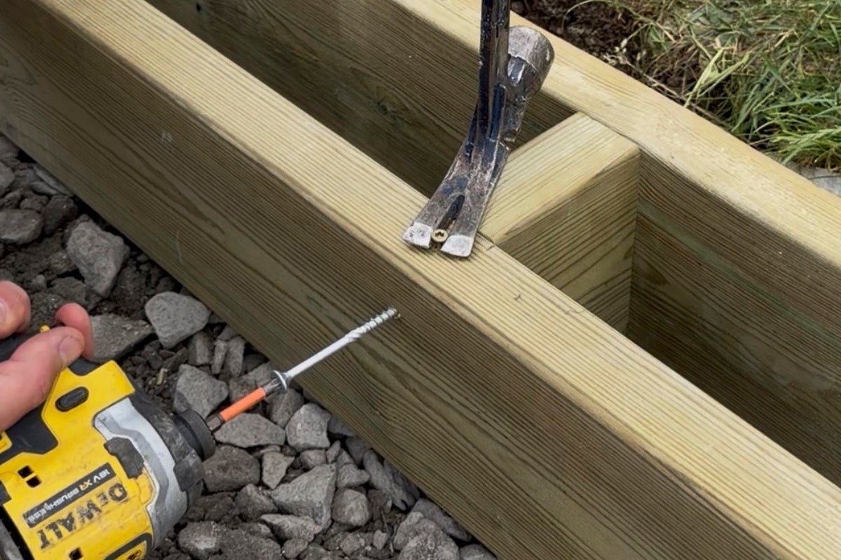 Träbjälkar skruvas ihop med en slagskruvdragare och DeWalt Logo, en hammare används som hävstång.