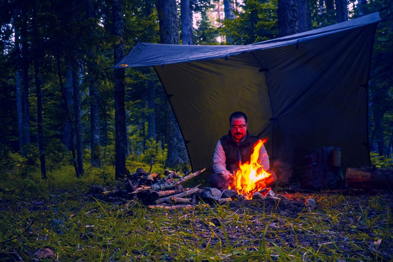 Skogsscen med man vid lägereld under en presenning