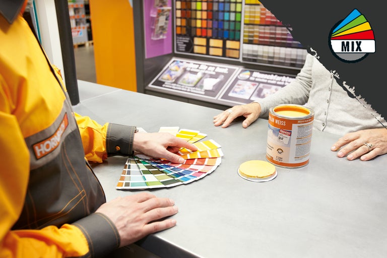 En Hornbach-anställd ger råd till en kund om färgval med en färgfläkt bredvid en färgblandningshink.