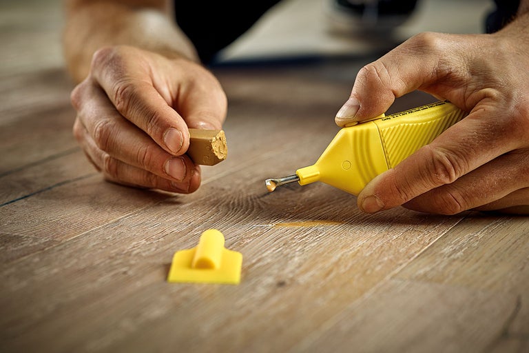 En person reparerar ett trägolv med ett reparationskit för trägolv.