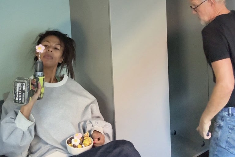 Kvinna håller i en sladdlös skruvdragare med borr och en skål med godis, medan en man monterar ett skåp i bakgrunden.