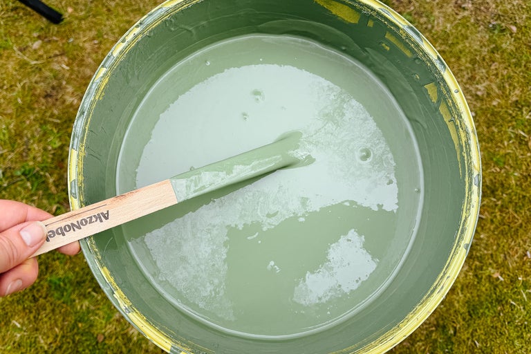 Hink med grön färg och omrörningspinne