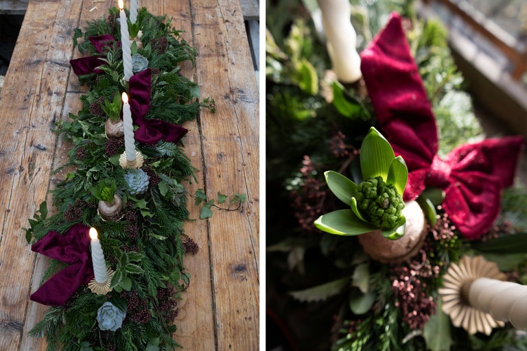 Festlig bordsdekoration med grangrönt, ljus och rosetter på ett träbord