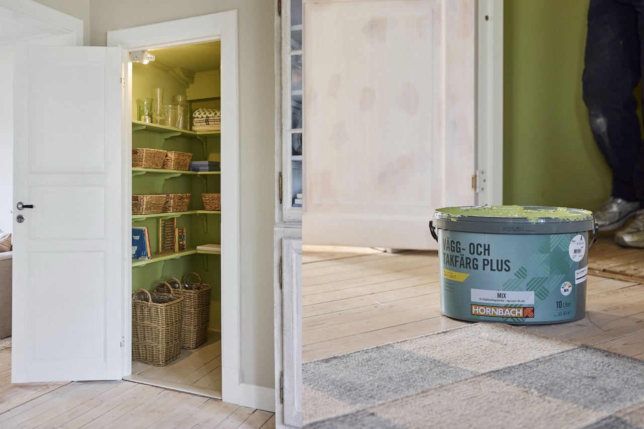 En 10-liters hink med Hornbach vägg- och takfärg plus bredvid en grönmålad skafferi med flätade korgar och hyllor.