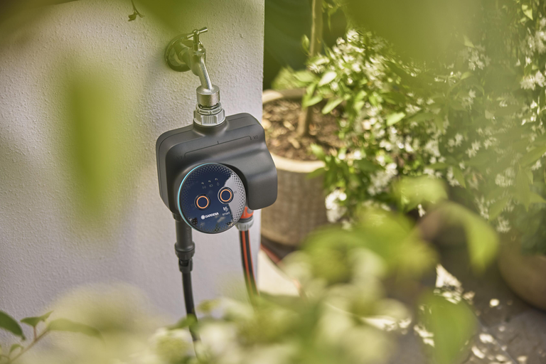 Gardena smart bevattningsdator monterad på en utomhuskran i trädgården för automatisk bevattning.