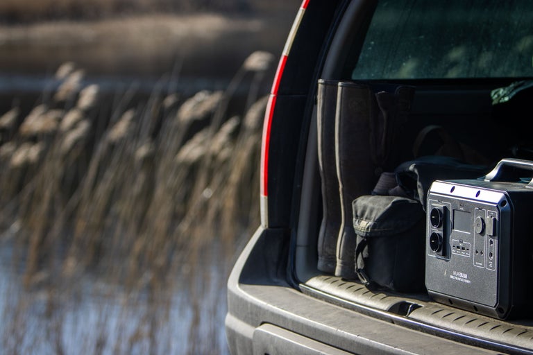 Bakre vy av en bil med gummistövlar, en väska och en bärbar kraftstation i bagageutrymmet