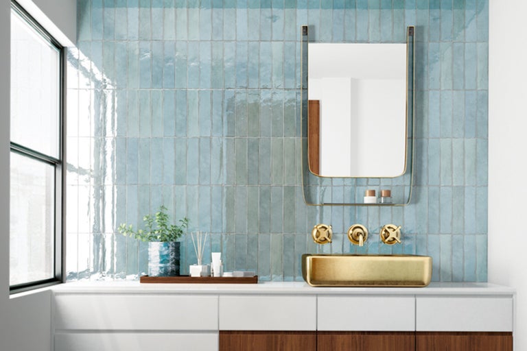 Badrum med blågrönt kakel, tvättställ, spegel och gyllene armatur