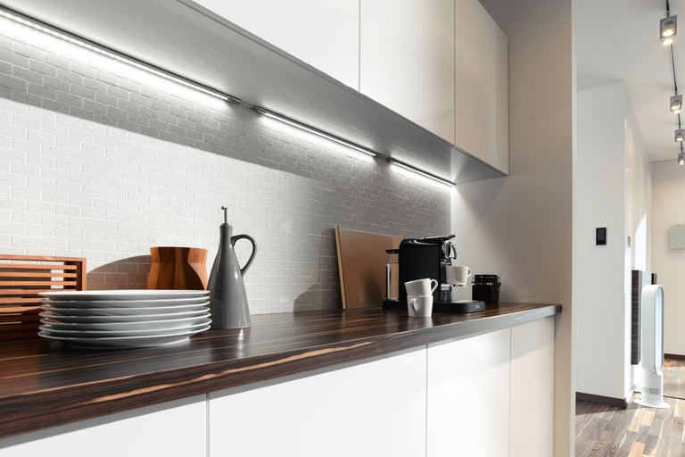 Modernt kök med vita skåp, mörk bänkskiva, mosaikplattor och LED-belysning.