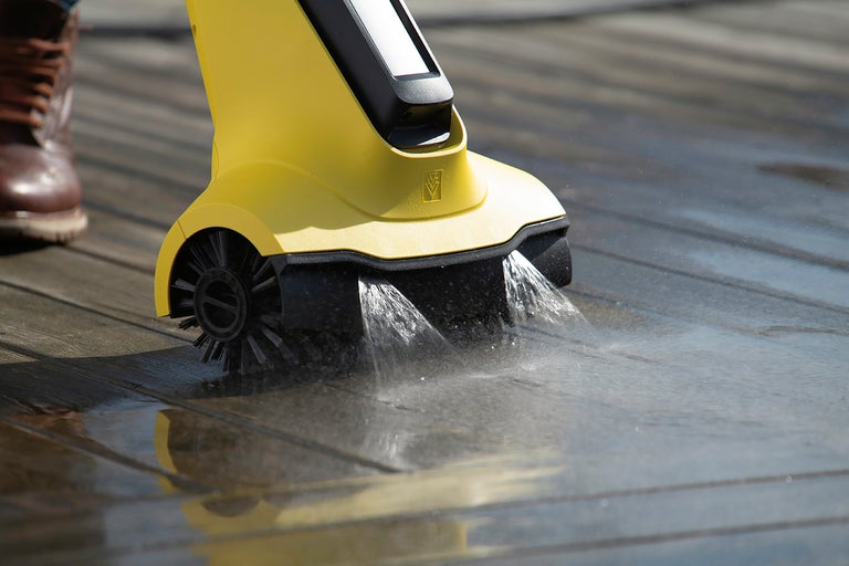 Elektrisk terrasstvätt med roterande borstar och vattenstrålar rengör en träterrass.