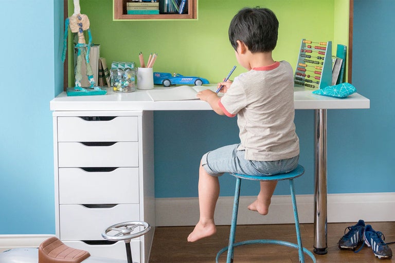 Barn sitter vid ett skrivbord och skriver i en anteckningsbok.