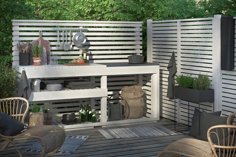 Utomhuskök med vit träpanel och diverse köksredskap på en terrass.