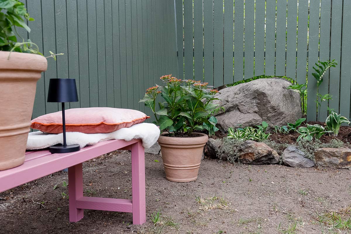 Anlagd trädgård med bänk, kuddar, blomkrukor och trädgårdsstaket