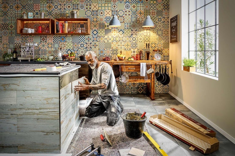 Man installerar väggpaneler i ett kök med mönstrat kakel