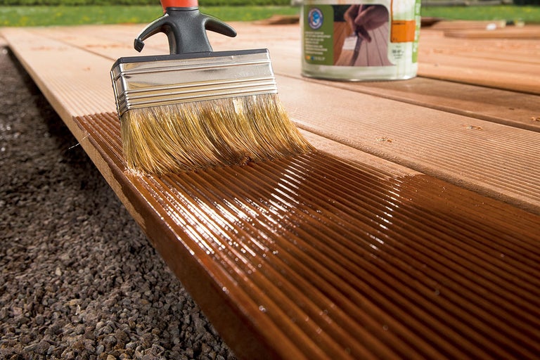 Pensel applicerar träskyddslasyr på en altanbräda