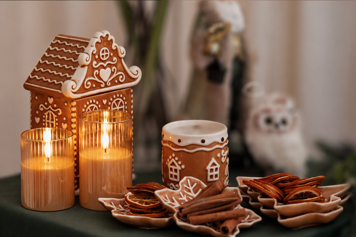 Julbordsdekoration med pepparkakshus, ljus i glas, kanelstänger och torkade apelsinskivor på stjärnformade fat.