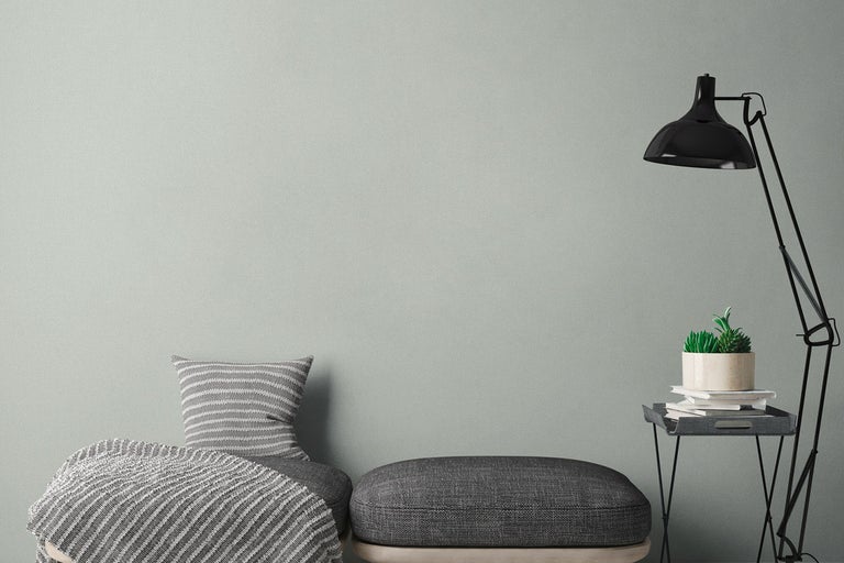 Vardagsrum med enfärgad tapet, kudde, pall och golvlampa