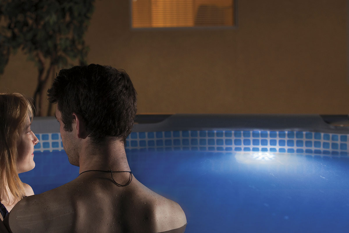 Scen med ett par i en pool med blå mosaikplattor och poolbelysning