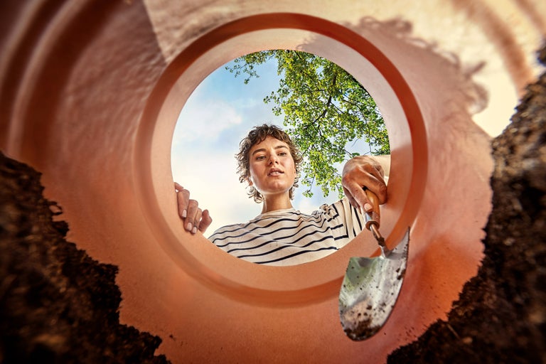 Vy från en planteringslåda på en kvinna med en planteringsspade och träd i bakgrunden.