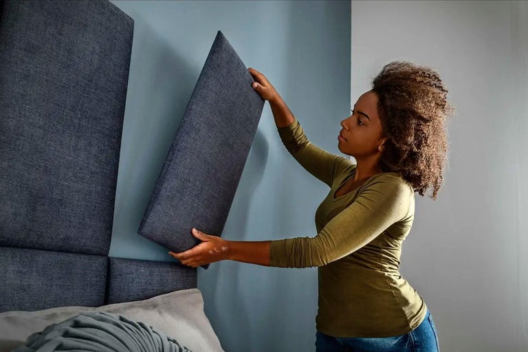 Kvinna fäster akustikpaneler på väggen i rummet.