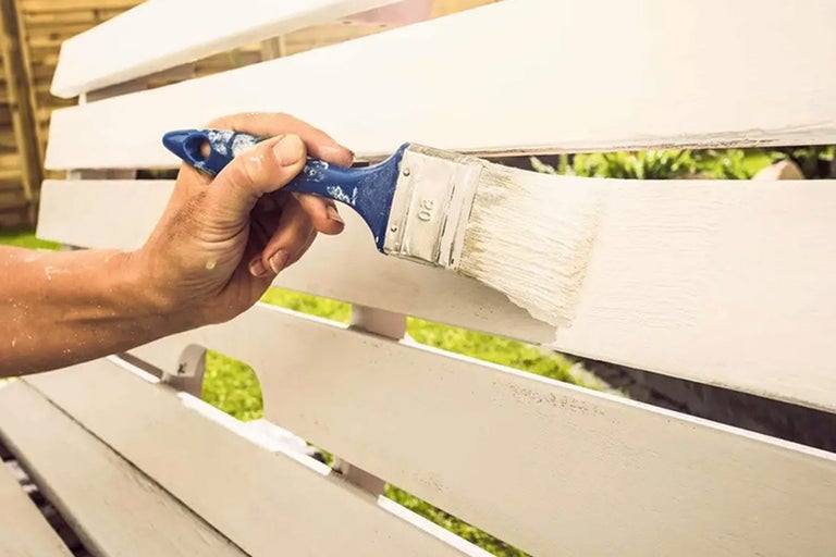 En person målar en träbänk med en pensel.