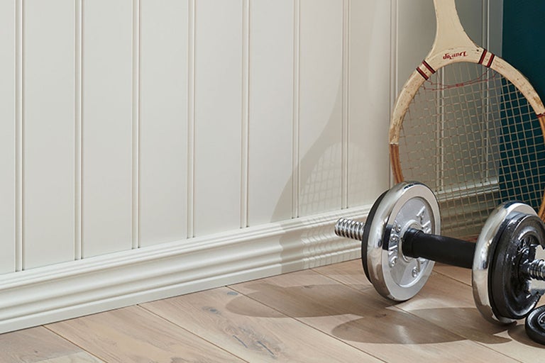 Ljus trävägg med spjälor och golvlister, hantel och tennisracket på trägolv