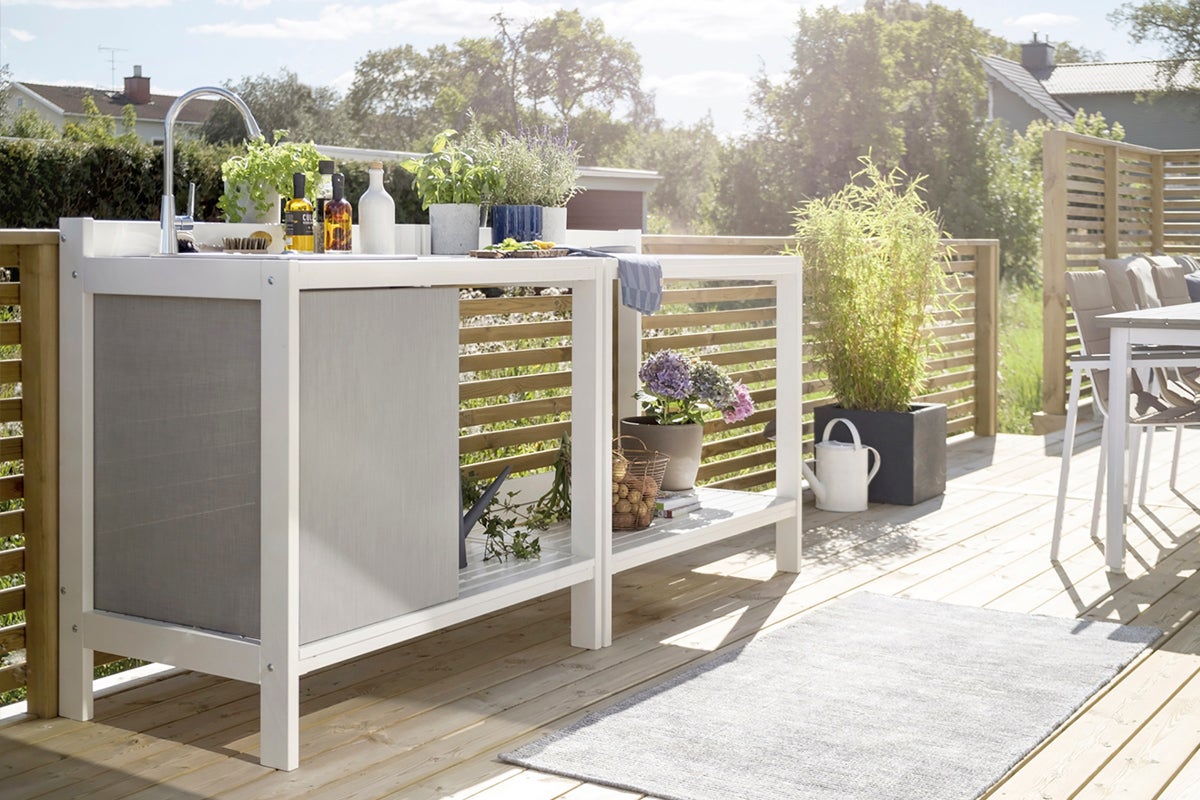 Trädgårdsscen med utekök, diskho, växter och trädgårdsdekoration på en träaltan.