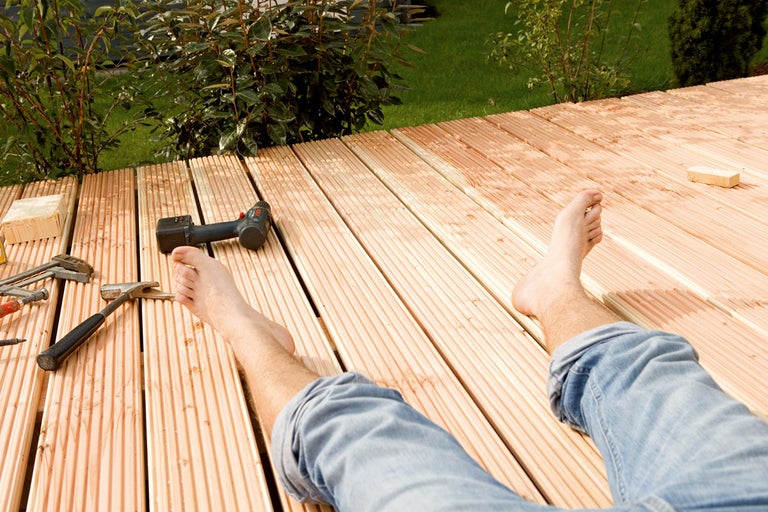Person ligger på trägolv med verktyg och borrmaskin