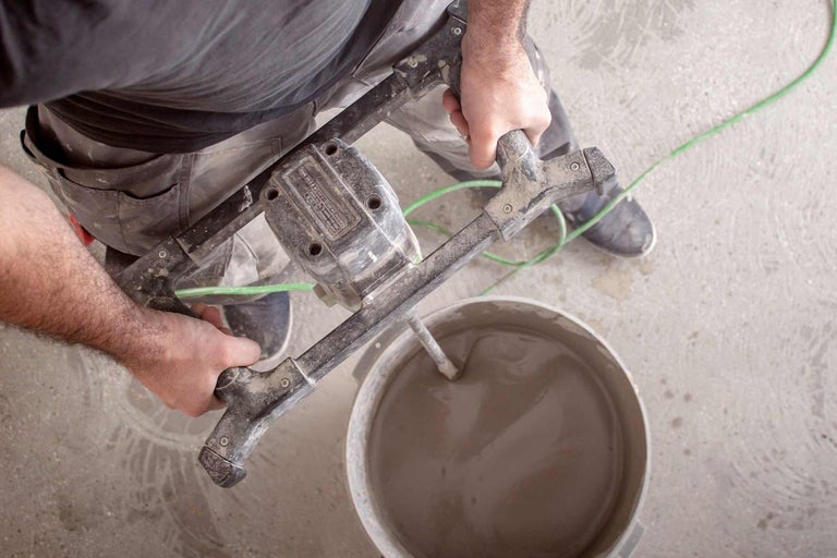 En hantverkare blandar murbruk med en elektrisk murbruksblandare i en hink.