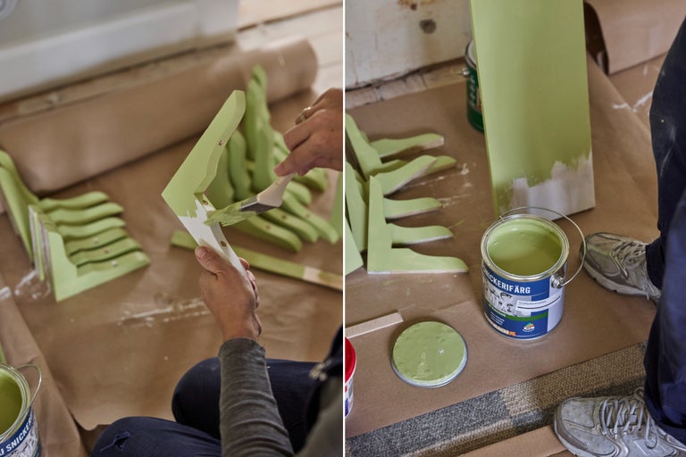 En person målar konsoler i trä med grön snickerifärg och en pensel bredvid en öppen färgburk.