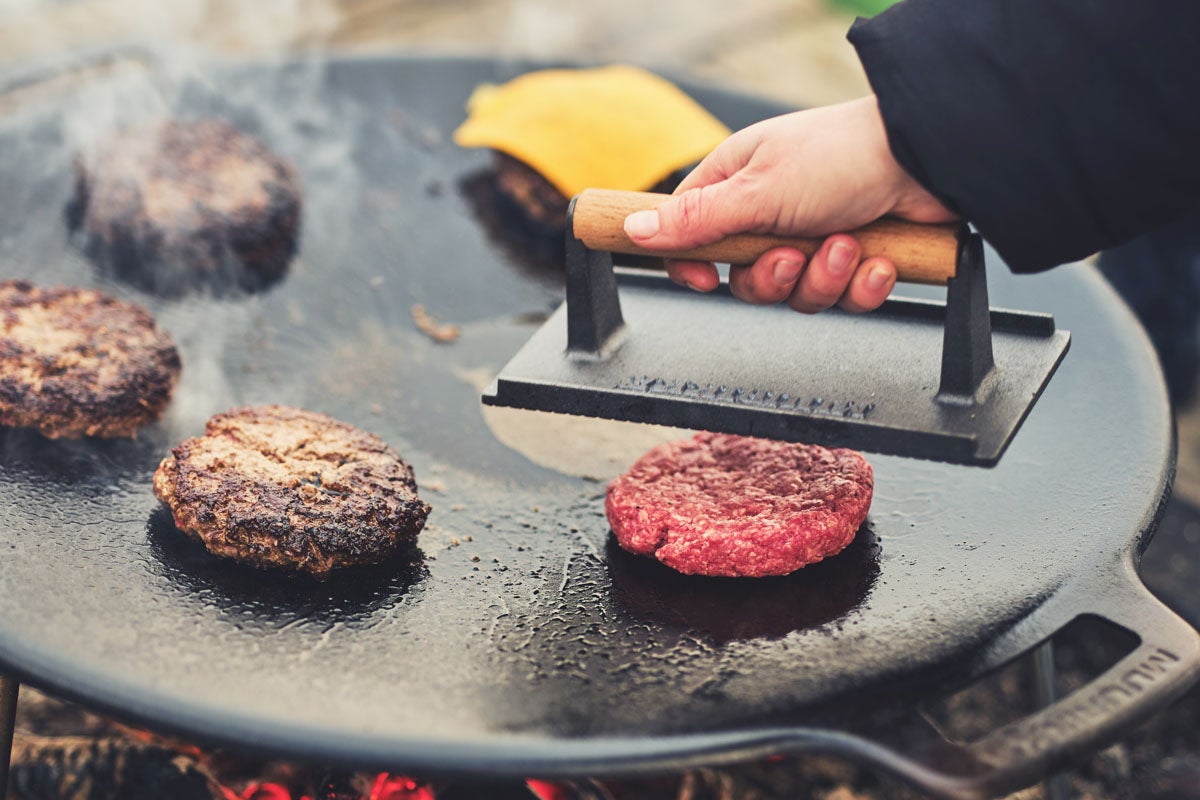 Hamburgare tillagas på en grillplatta med en grillpress.