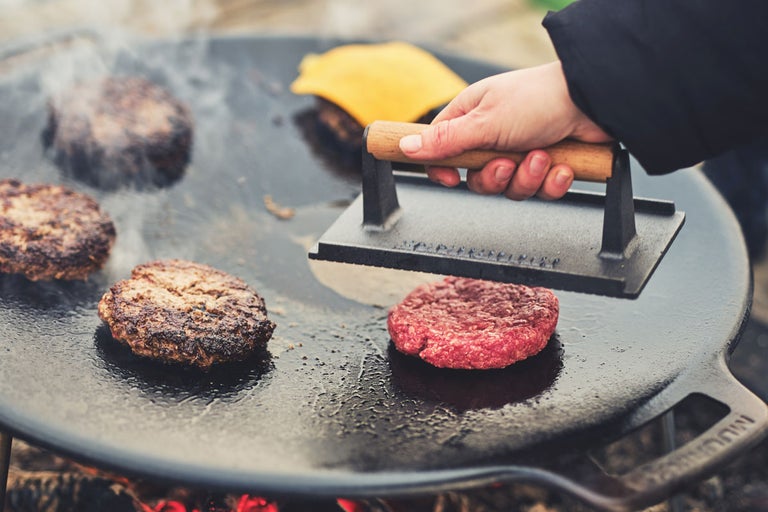 Hamburgare tillagas på en grillplatta med en grillpress.