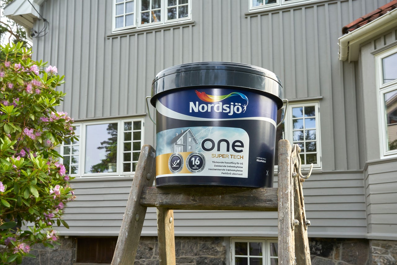 En burk Nordsjö One Super Tech fasadfärg står på en stege framför ett hus.