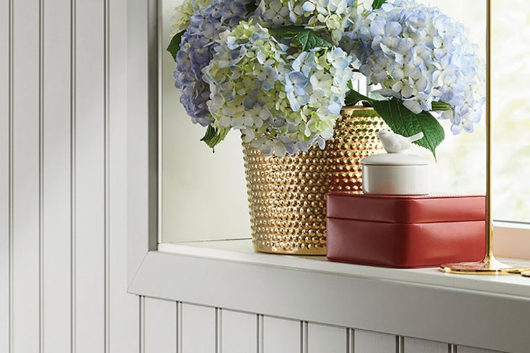 Dekorativa blommor i en gyllene vas på en fönsterbräda