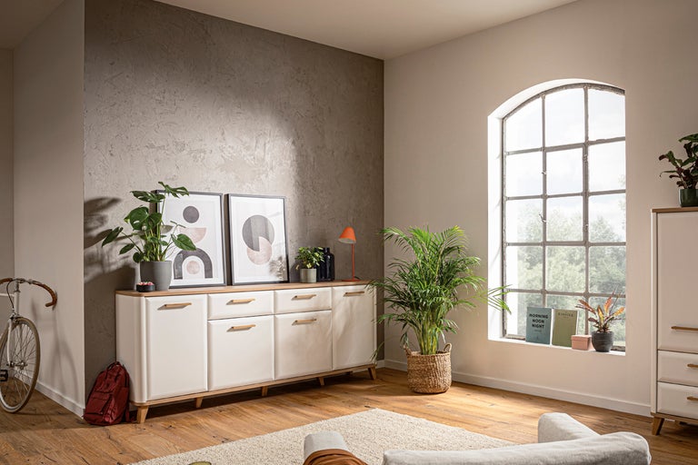 Vardagsrum med byrå, växter, tavlor och fönster