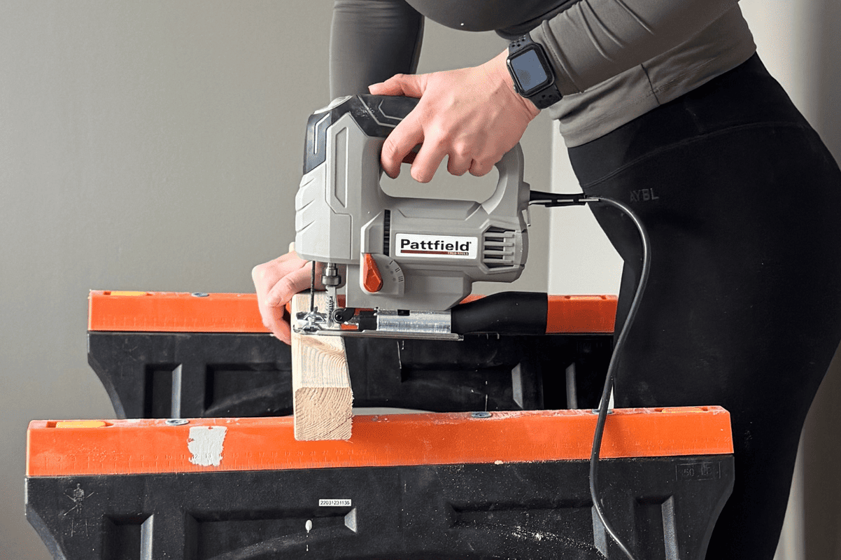En person använder en Pattfield sticksåg för att såga en träbit som ligger på två arbetsbänkar.