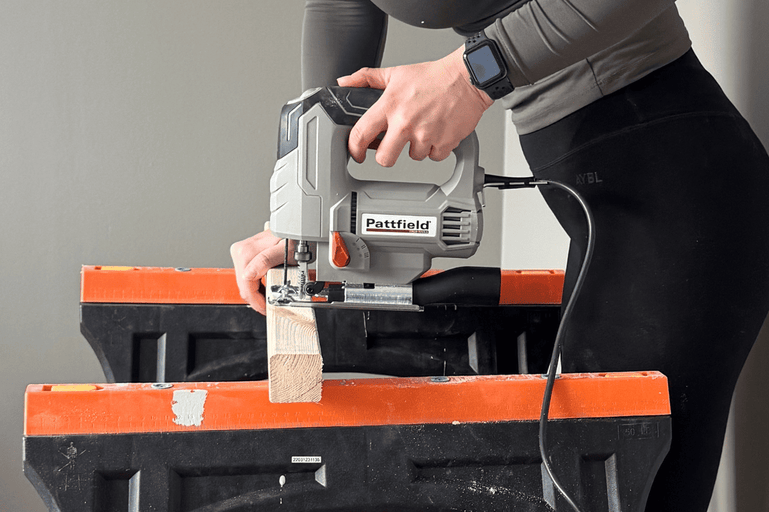 En person använder en Pattfield sticksåg för att såga en träbit som ligger på två arbetsbänkar.