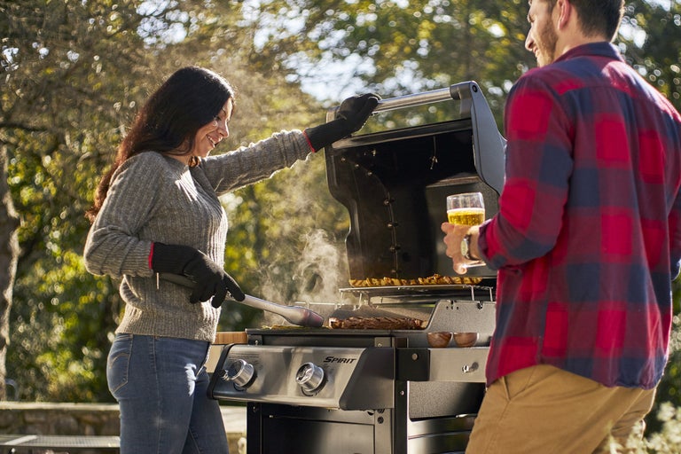 Grillscen med kvinna som vänder kött på en grill och man med en öl