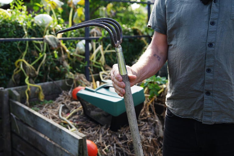 En person håller en grep i en trädgård med en komposthög.
