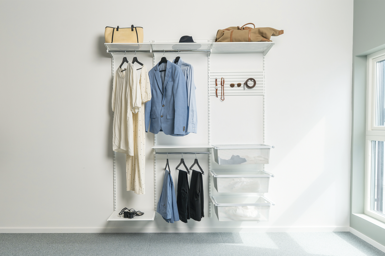 Vägghyllsystem med klädstänger, hyllplan, perforerad platta och lådor för organiserad förvaring av kläder och accessoarer.