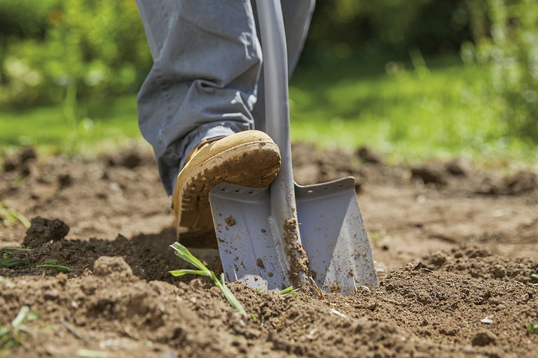 Närbild av en person som trycker ner en spade i marken.