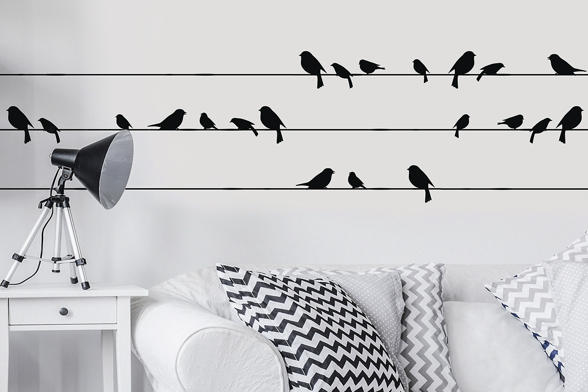 Väggdekoration med fågelmotiv på elledningar ovanför soffa och lampa