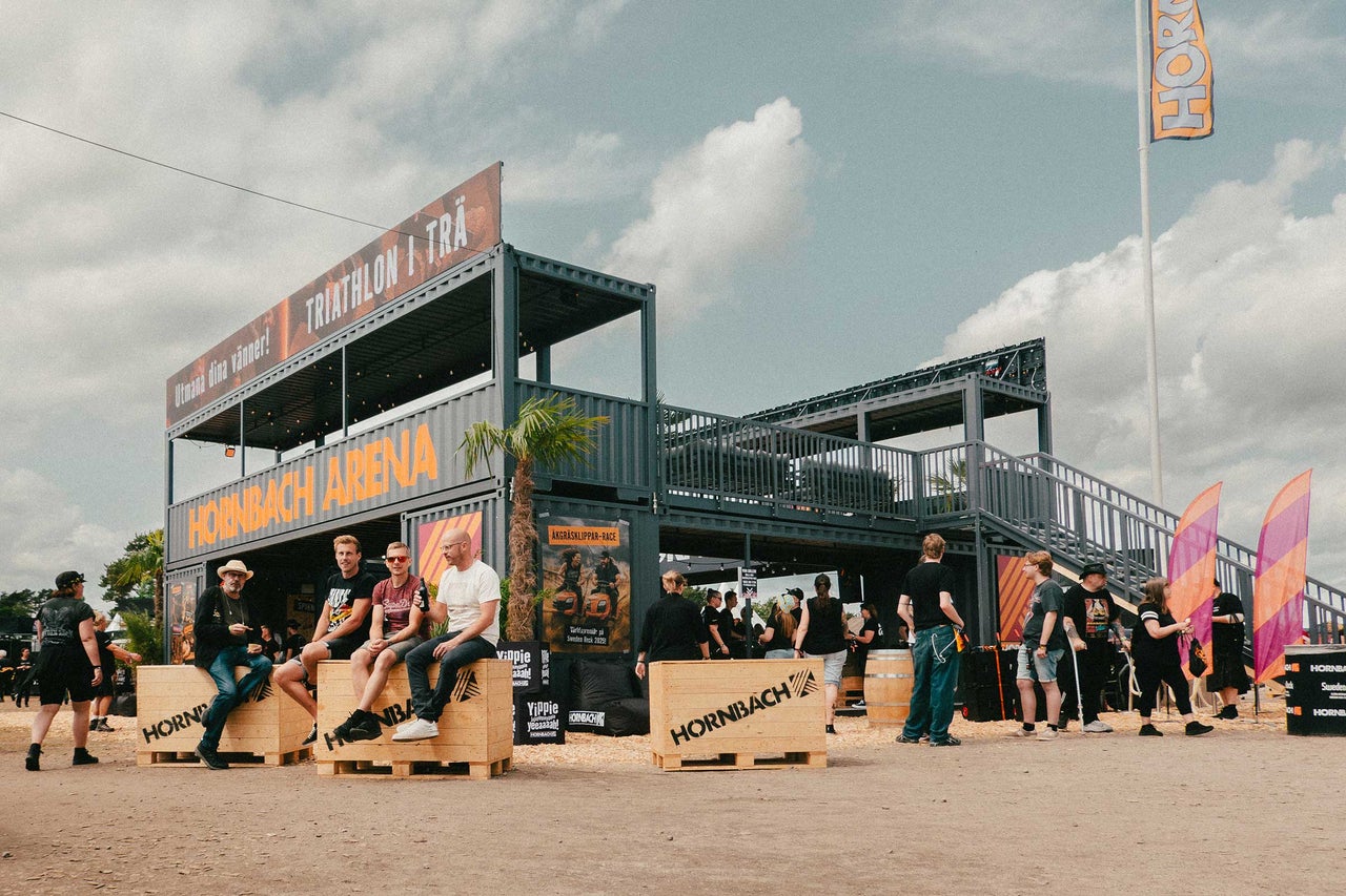 Tvåvånings Hornbach Arena av containrar på ett evenemang med besökare och träboxar med Hornbach Logo.